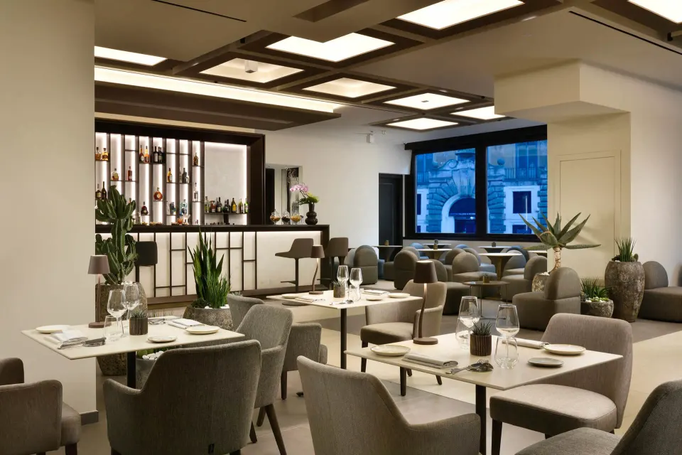 A bright dining room with set tables, grey upholstered chairs and a coffered ceiling.